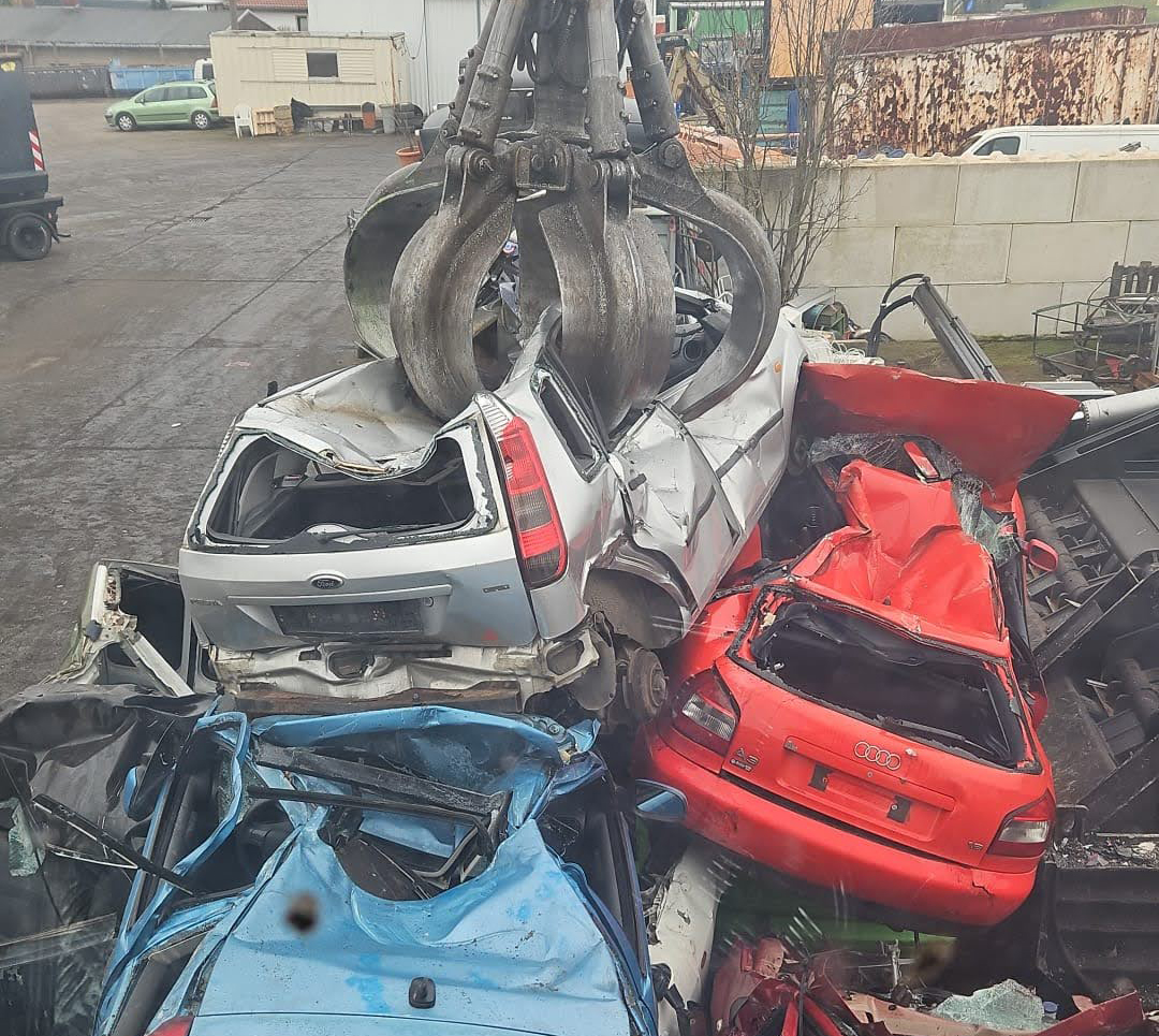 Kran verlädt Schrottautos in die Schrottpresse